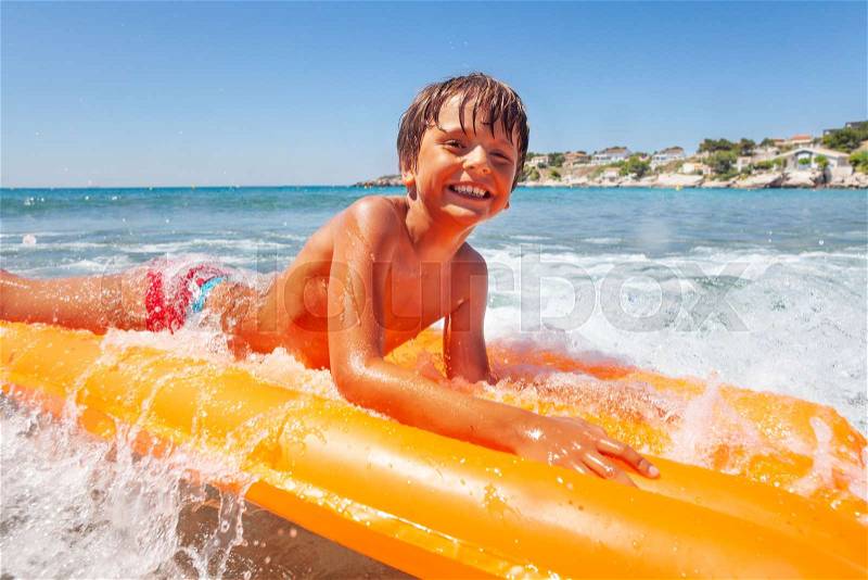 Portrait of cute boy riding the waves on big swimming mattress, spending summer vacation at the seaside, stock photo