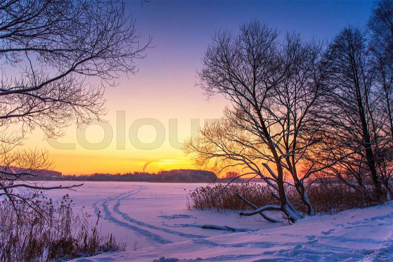 Sunset winter landscape with snow-covered lake in violet and pink colors. Beautiful colorful winter sunset with frozen lake and sunset sky. Winter park. Belarus, stock photo