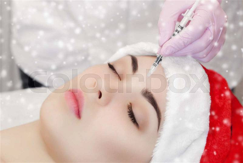The doctor cosmetologist makes injection on the face skin and lips of a beautiful, young woman in the Santa Claus hat. New Year\'s and Cosmetology concept, stock photo