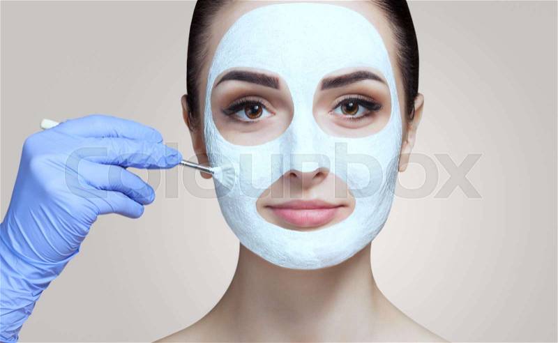 The cosmetologist for the procedure of cleansing and moisturizing the skin, applying a mask with stick to the face of a young woman in beauty salon. Cosmetology and ..., stock photo