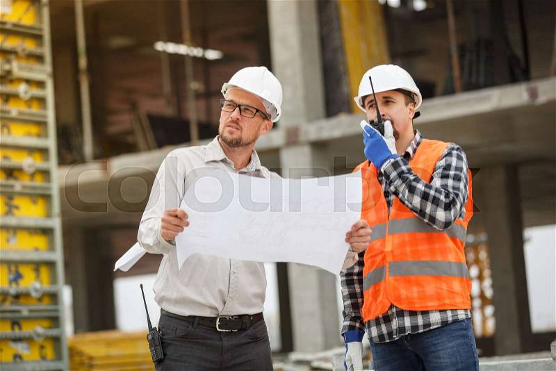 Male architect and developer with walkie talkie discussing blueprints of an architect project at , stock photo