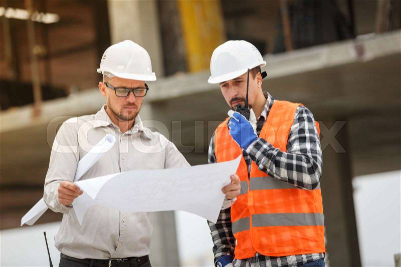 Male architect and developer with walkie talkie discussing blueprints of an architect project at , stock photo