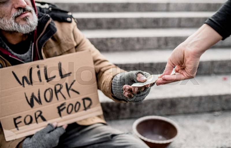A midsection view of woman giving money to homeless beggar man sitting in city, stock photo