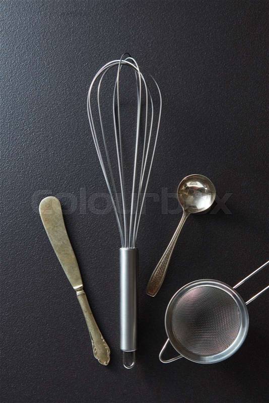 Set of kitchen tools knife, whisk, sieve and spoon on black concrete background with copy space. Top view, stock photo