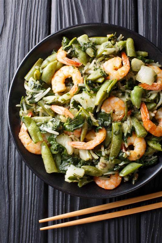 Chinese traditional Stir frying of shrimp, spinach, soy sprouts, pea pods and pak choi close-up on a plate on the table. Vertical top view from above, stock photo