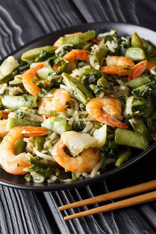 Stir fry of shrimp with spinach, soy sprouts, pea pods and pak choi close-up on a plate. vertical, stock photo