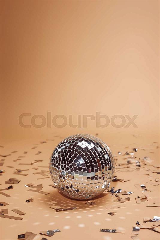Shiny silver disco ball and confetti on beige, stock photo