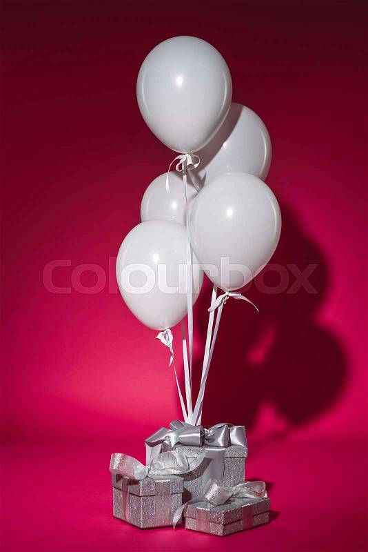 Bundle of white balloons and silver gift boxes on burgundy, stock photo