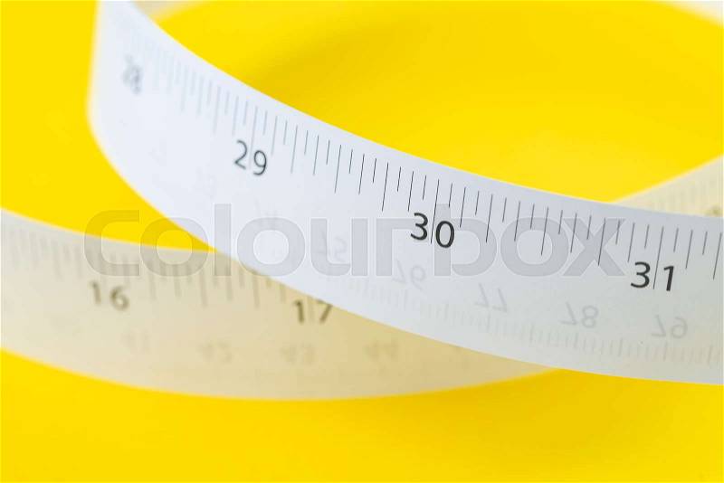 White measuring tapes with centimeter and inches on vivid yellow background for presentation, length, long, fitness, diet or maker instrument and tools concept, stock photo
