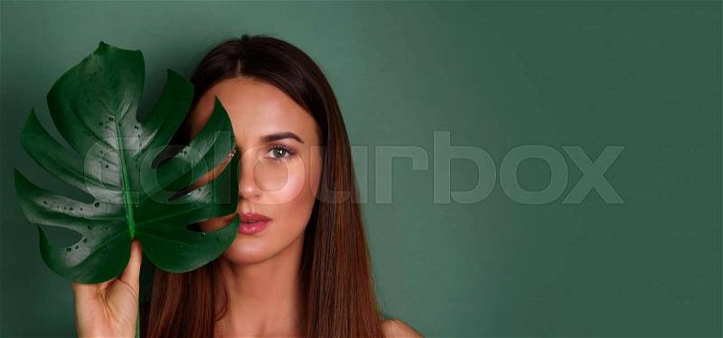 Young woman with natural make up and tropical monstera leaf in hand over green background with copy space. Skin care, pure beauty, body treatment, cosmetics concept. ..., stock photo