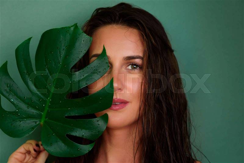 Young girl with wet hair, natural make up holding tropical monstera leaf on green background. Banner, copy space. Skin care, pure beauty, body treatment, fashion, ..., stock photo