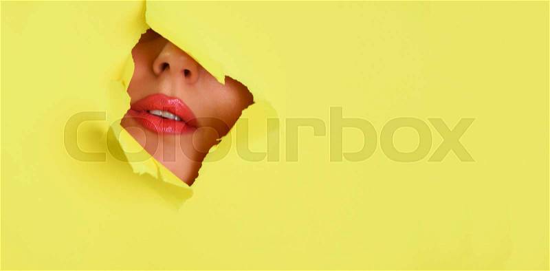 View of bright lips through hole in yellow paper background. Make up artist, beauty concept. Cosmetics sale. Beauty salon advertising banner with copy space, stock photo