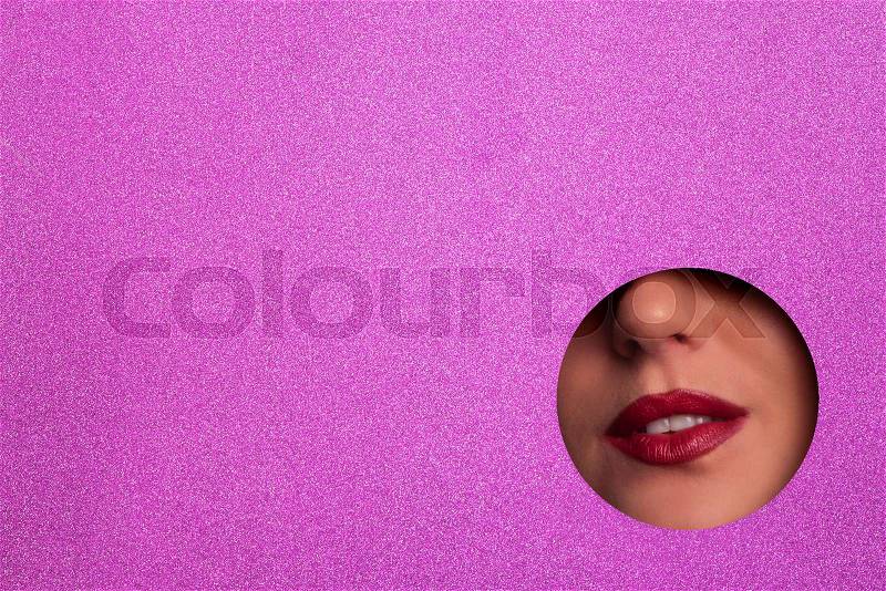 View of bright lips through hole in shimmer violet paper background. Make up artist, beauty concept. Ready to new year party. Cosmetics sale. Beauty salon ..., stock photo