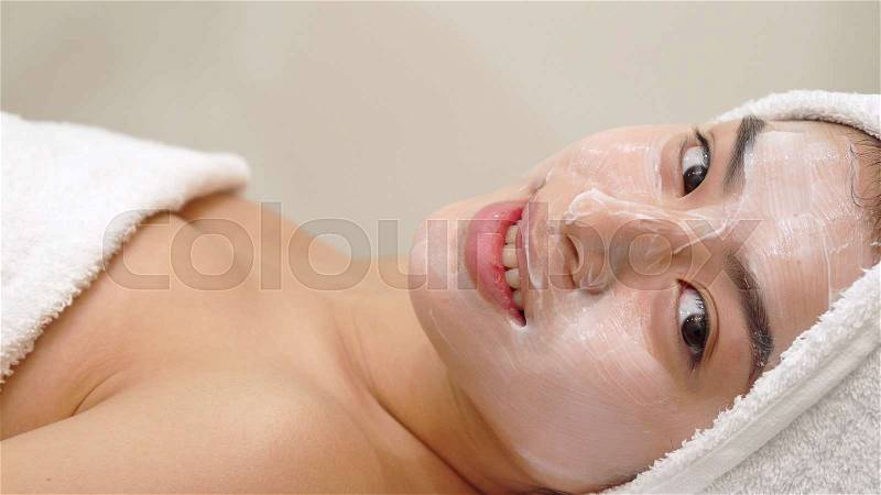 Pretty asian girl getting facial mask at the salon. Side view of cosmetologist applying anti-aging treatment on female face. Beauty specialist moving cosmetic brush ..., stock photo