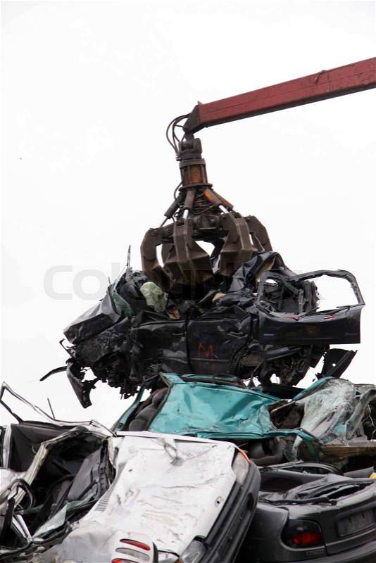 Car wreck being lifted by grab crane to be scrapped with other cars and scrapped cars around, stock photo