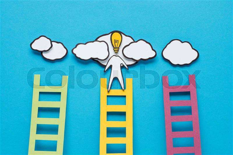 Cardboard man with light bulb head climbing one of three ladders on blue background, ideas concept, stock photo