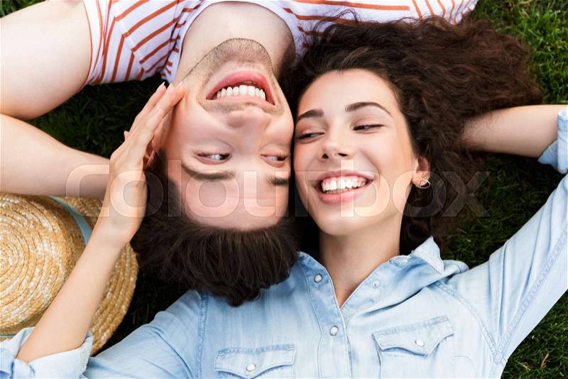 Image from top of beautiful people man and woman 20s, lying alongside opposite heads on green grass in park, stock photo