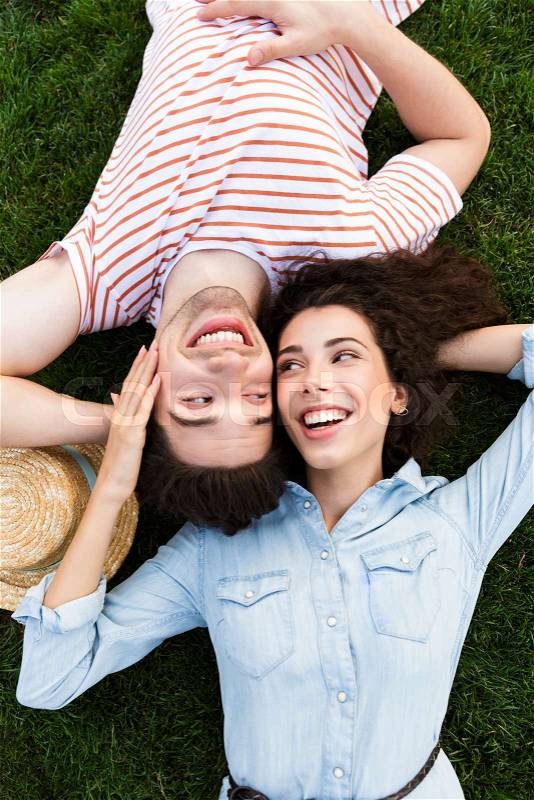 Image from top of loving people man and woman 20s, lying alongside opposite heads on green grass in park, stock photo