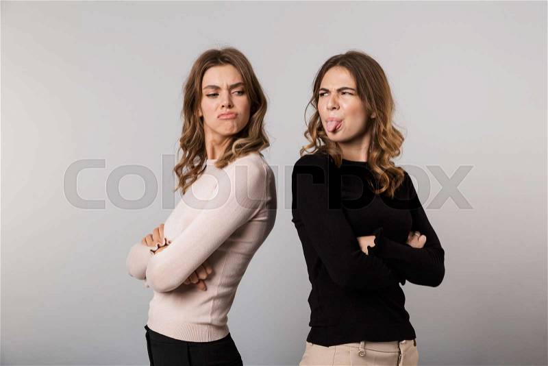 Image of two upset girls standing back to back with arms crossed and expressing resentment, isolated over gray background, stock photo