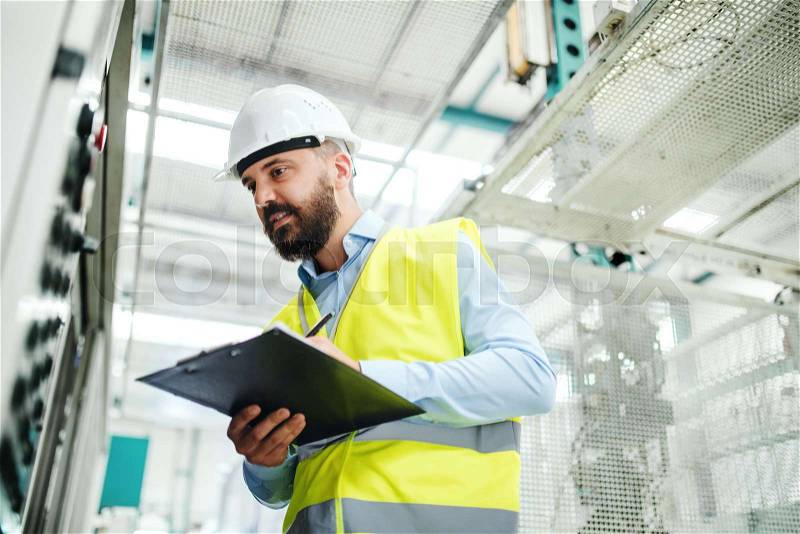 A portrait of a mature industrial man engineer with clipboard in a factory, working. Copy space, stock photo
