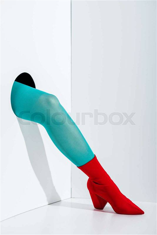 Cropped image of girl showing leg in stylish turquoise tights and red shoe in hole on white, stock photo