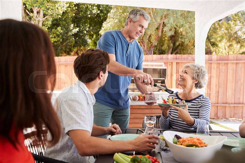 Senior dad serving his wife food at a family barbecue, stock photo