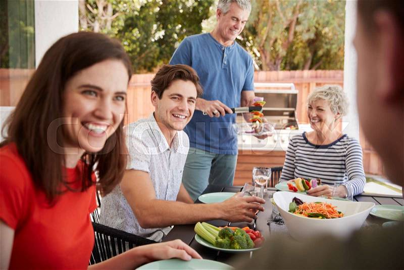 Senior dad serving his family food at barbecue in the garden, stock photo