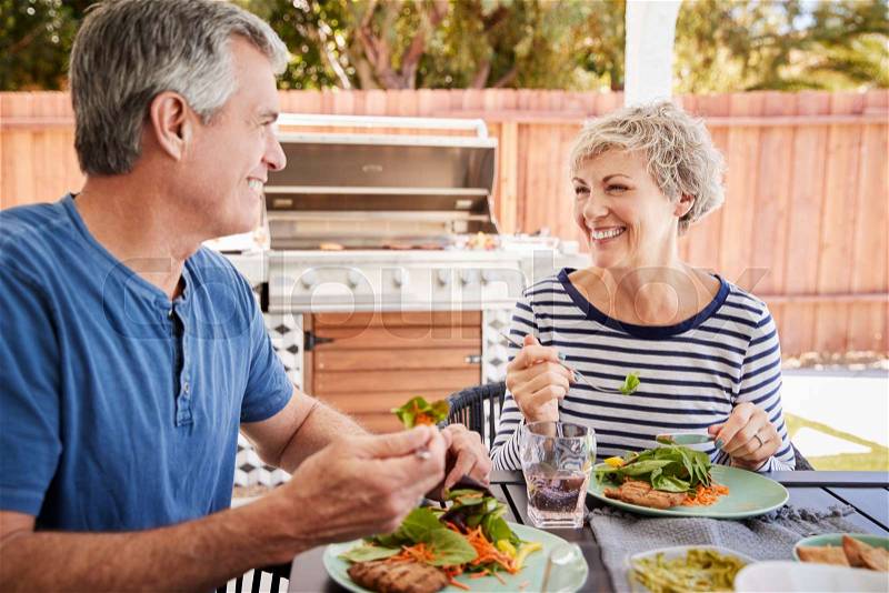 Senior white couple eating together at a table in the garden, stock photo