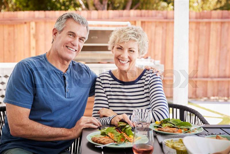 Senior white couple sit at lunch in garden looking to camera, stock photo