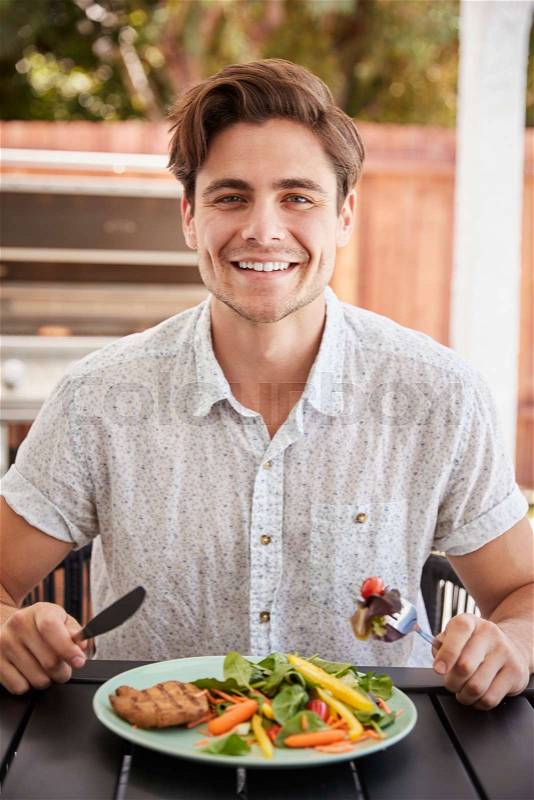 Young white man eating lunch at a table in the garden, stock photo
