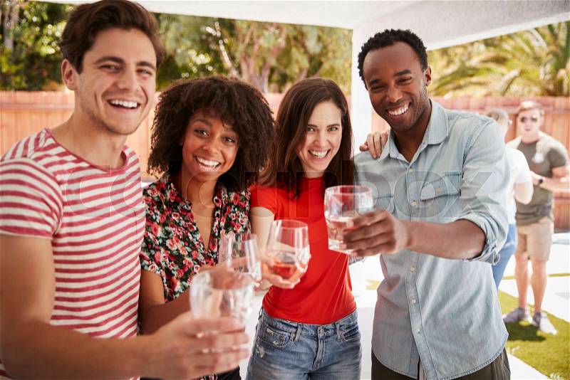 Adult friends at a backyard party raising glasses to camera, stock photo
