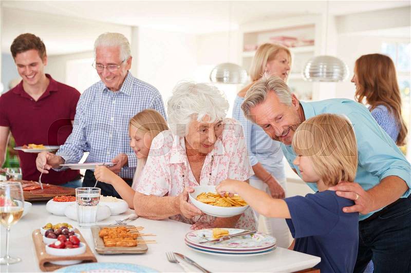 Multi-Generation Family And Friends Eating Food In Kitchen At Celebration Party, stock photo