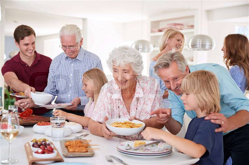 Multi-Generation Family And Friends Eating Food In Kitchen At Celebration Party, stock photo