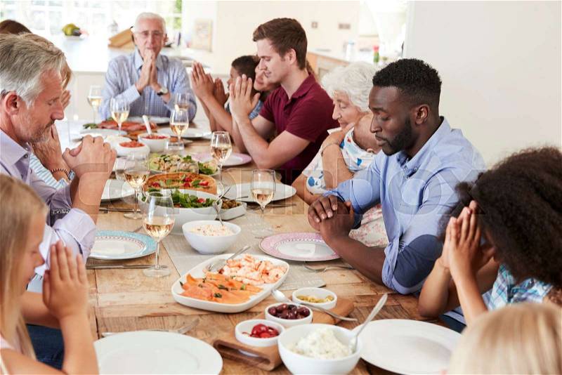 Multi-Generation Family And Friends Around Table Praying Before Meal At Party, stock photo