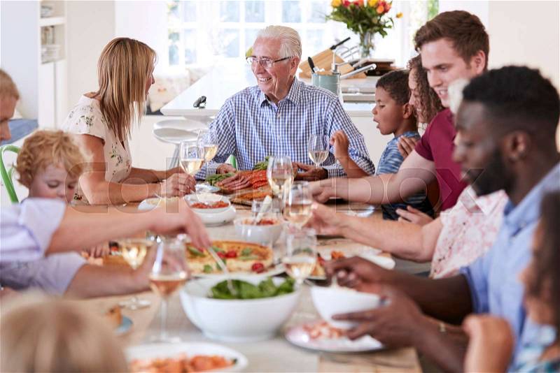 Group Of Multi-Generation Family And Friends Sitting Around Table And Enjoying Meal, stock photo