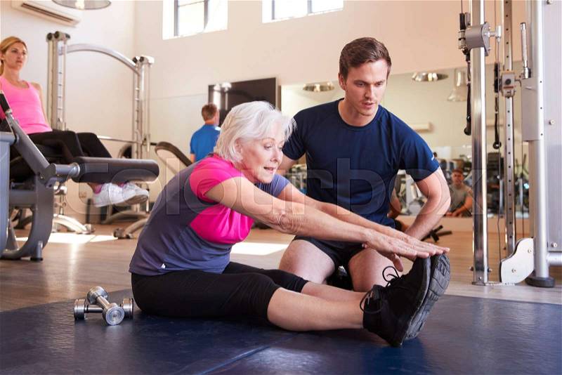 Senior Woman Exercising In Gym Being Encouraged By Personal Trainer, stock photo