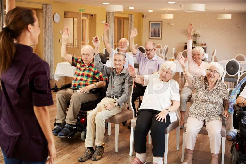 Carer Leading Group Of Seniors In Fitness Class In Retirement Home, stock photo