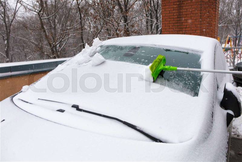 The long folding green brush cleans snow from a windshield of the car, stock photo