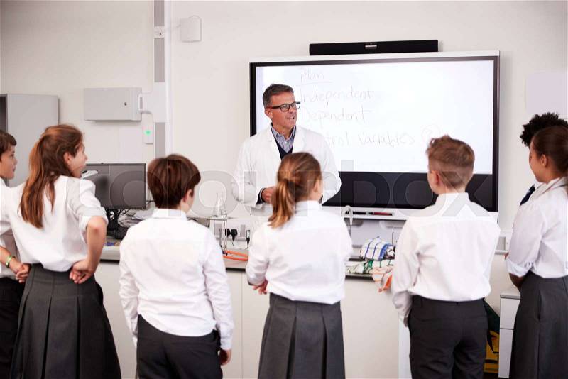 Male High School Tutor Teaching High School Students Wearing Uniforms In Science Class, stock photo