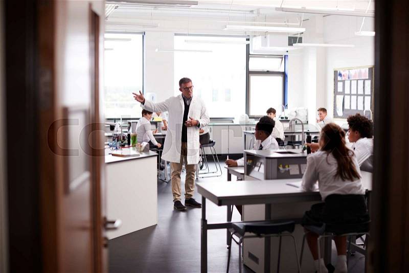 Male High School Tutor Teaching High School Students Wearing Uniforms In Science Class, stock photo