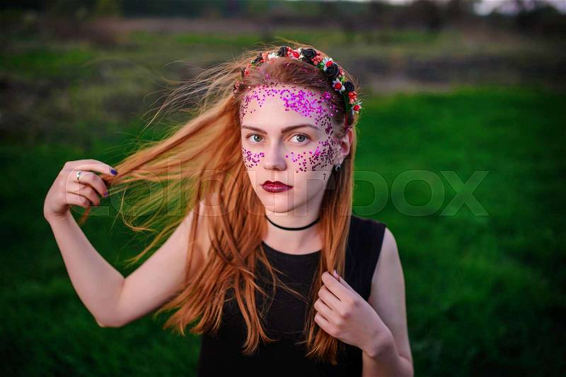 A young beautiful woman with a violet shine on her face standing on the grass and looking at the camera, stock photo