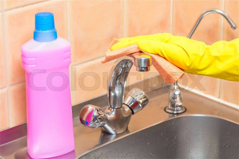 Woman cleans the tap in the kitchen with a rag, hands in yellow gloves close-up, stock photo