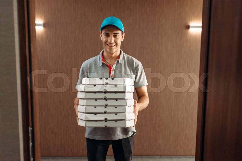 Pizza delivery man with boxes, delivering service. Courier from pizzeria holds cardboard package indoors, stock photo