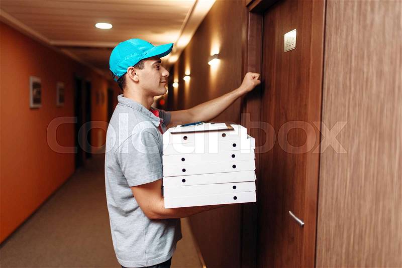 Pizza delivery boy knocking on the door of the customer, delivering service. Courier from pizzeria holds cardboard packages indoors, stock photo