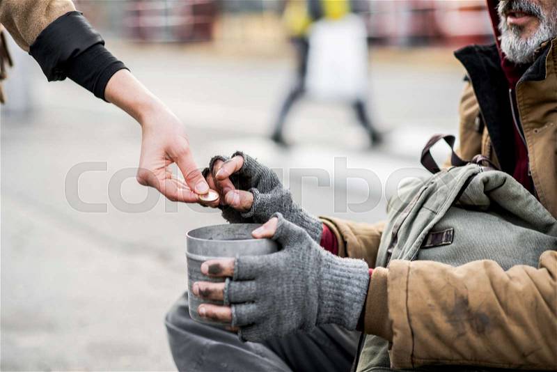 A midsection view of woman giving money to homeless beggar man sitting in city, stock photo