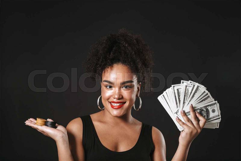 Image of a happy african woman posing isolated over black wall holding money and chips, stock photo