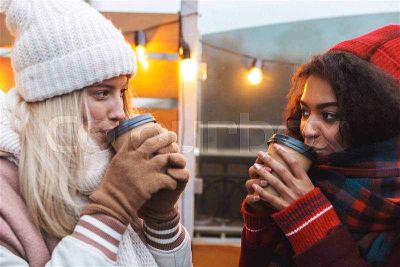 Image of a happy young friends girls talking with each other drinking coffee outdoors winter concept, stock photo