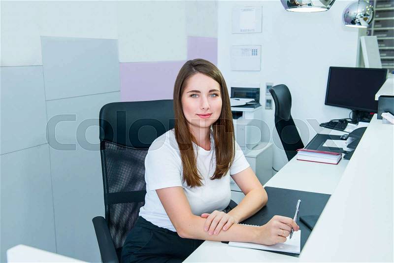 Portrait of skilled administrative manager sitting on her office workplace and making notes. Satisfied with occupation, young female receptionist, personal ..., stock photo