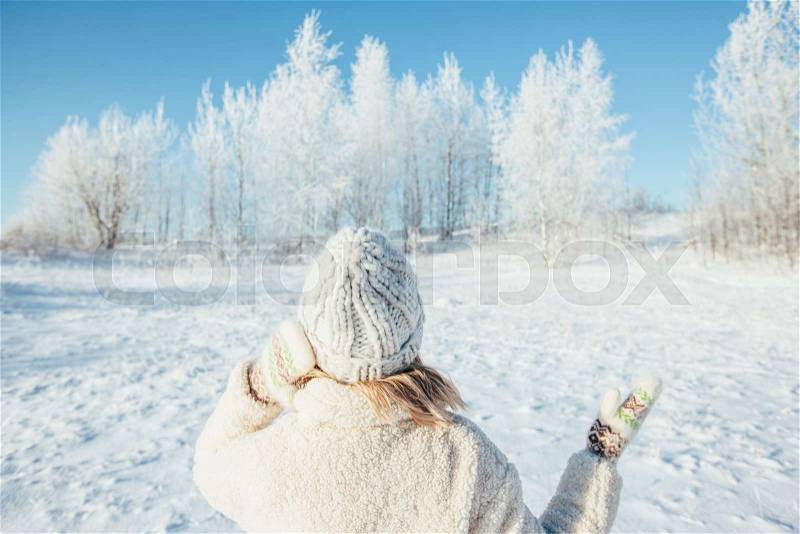 Photo of woman in fur coat, gloves and knitted hat standing and looking at snowy forest in magic winter day, stock photo