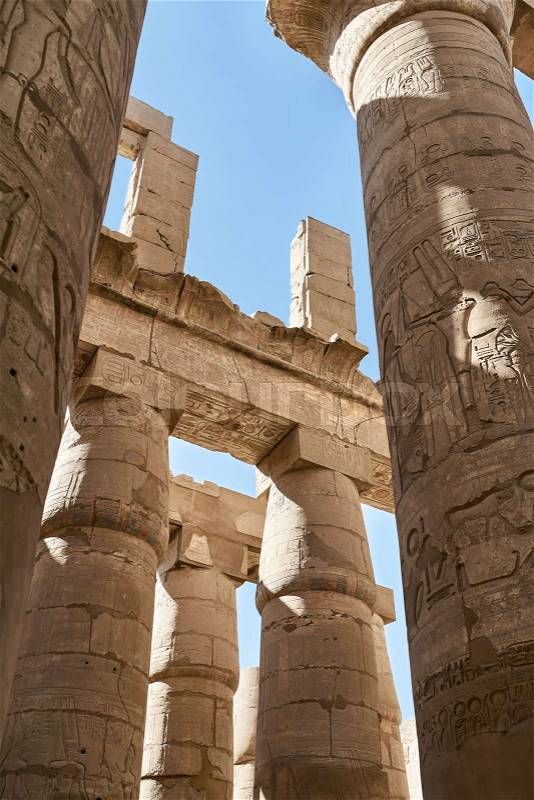 Part of Karnak Temple with ancient columns with egyptian hieroglyphs on the blue sky background in Egypt. Sun shines onto them. Vertical, stock photo
